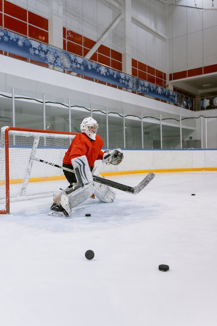 Hockey goalie in protective gear defends goal on indoor ice rink during game.