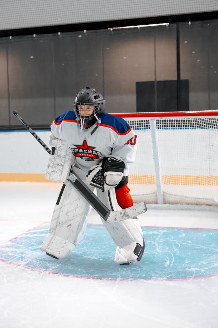 Teenage ice hockey goalie on ice rink, equipped with safety gear and ready to block shots.