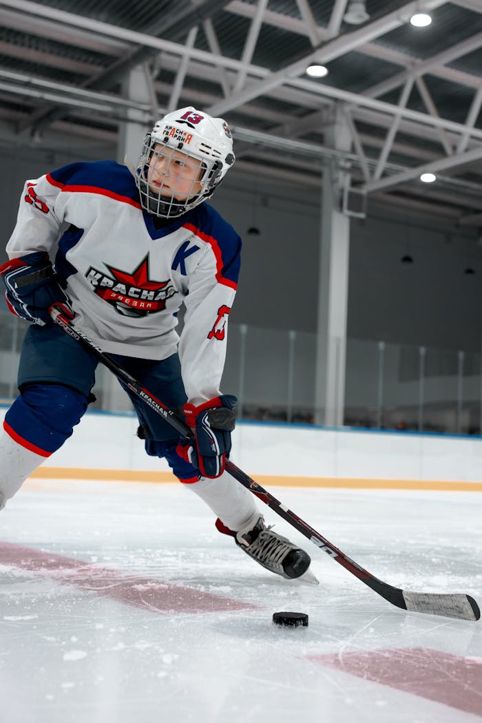Young hockey player in full gear skates with intensity on ice rink.